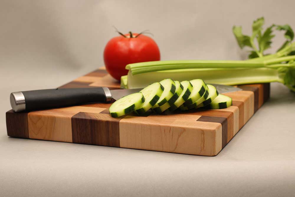 Maple, walnut, and cherry wood cutting board with knife and assorted vegetables