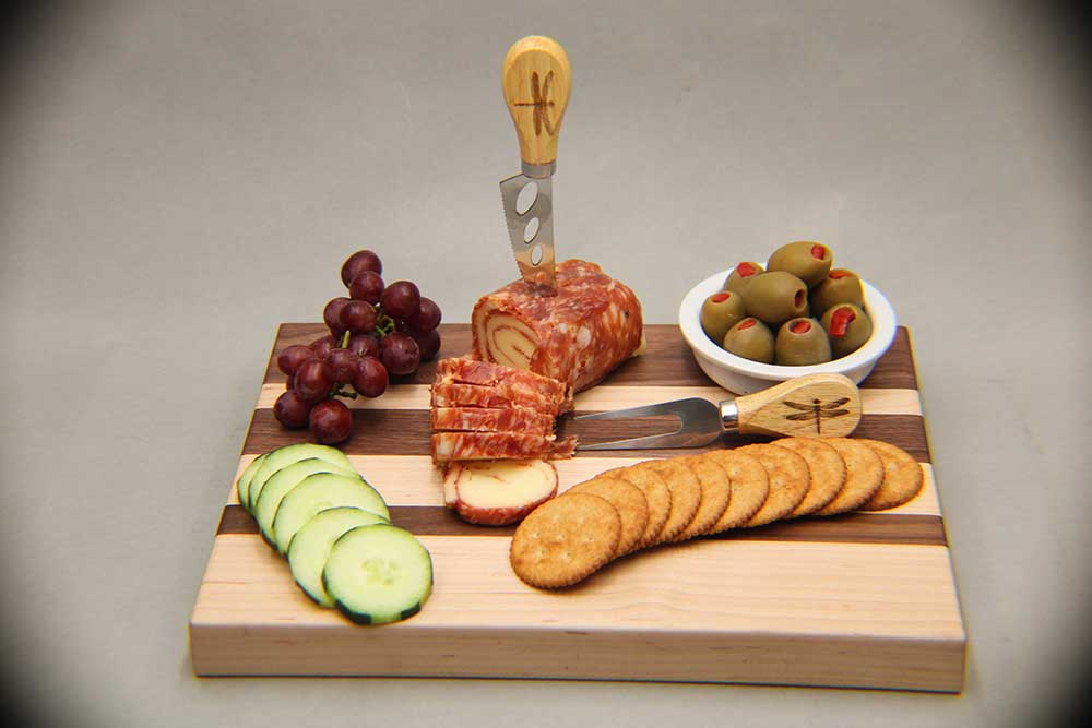 Walnut and maple charcuterie board with cutlery salami and cheese pinwheel and assorted fruits and vegetables dragonfly wood arts